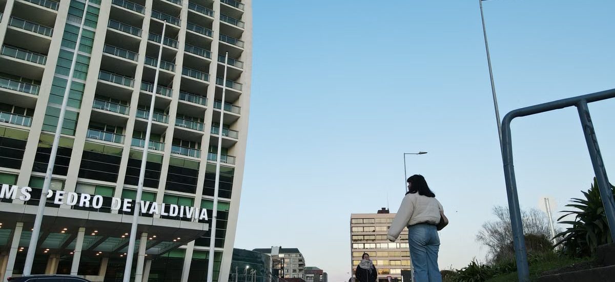 A modern urban street scene in Valdivia with pedestrians and high-rise building under clear sky.