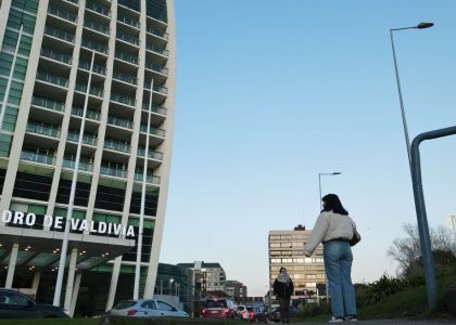 A modern urban street scene in Valdivia with pedestrians and high-rise building under clear sky.